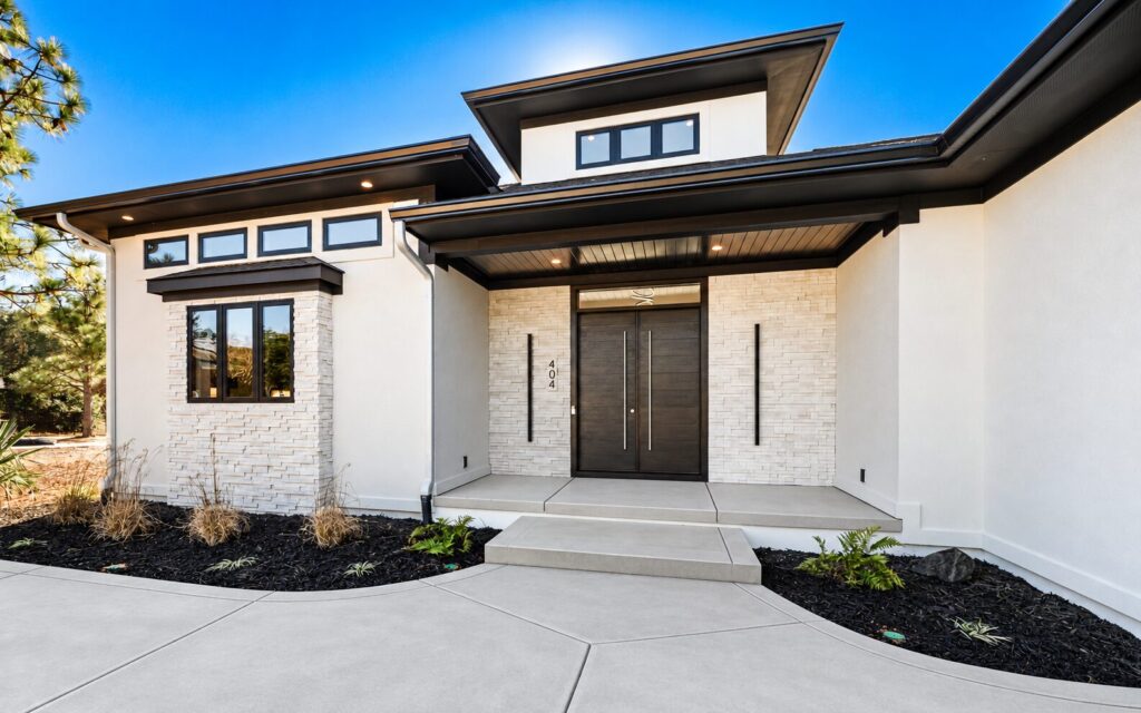 Contemporary custom home entrance in Seven Lakes, NC with pale concrete, white stone, black trim and pines