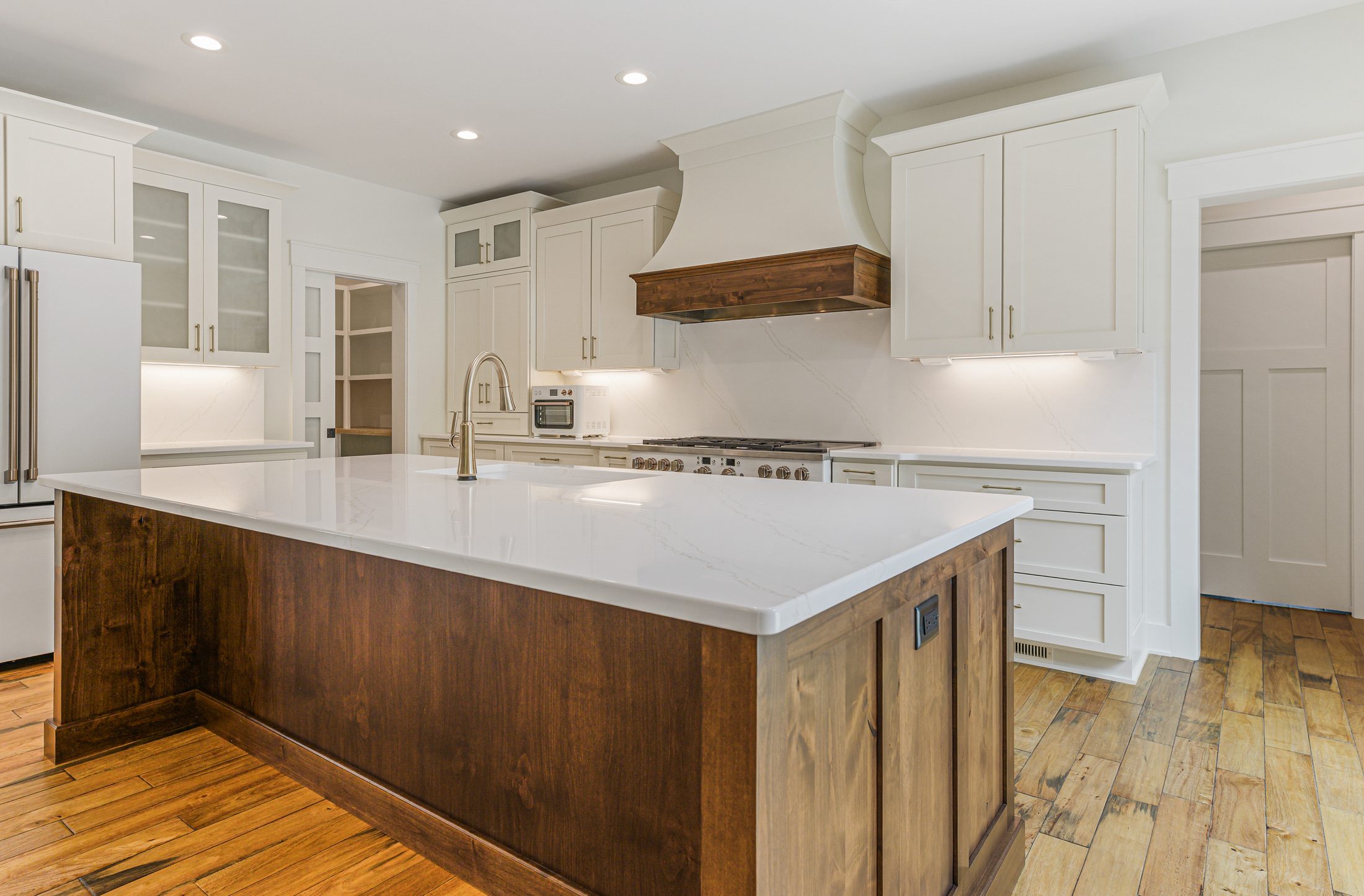 Kitchen island and custom wood range hood in a Arbor Creek custom home in West End