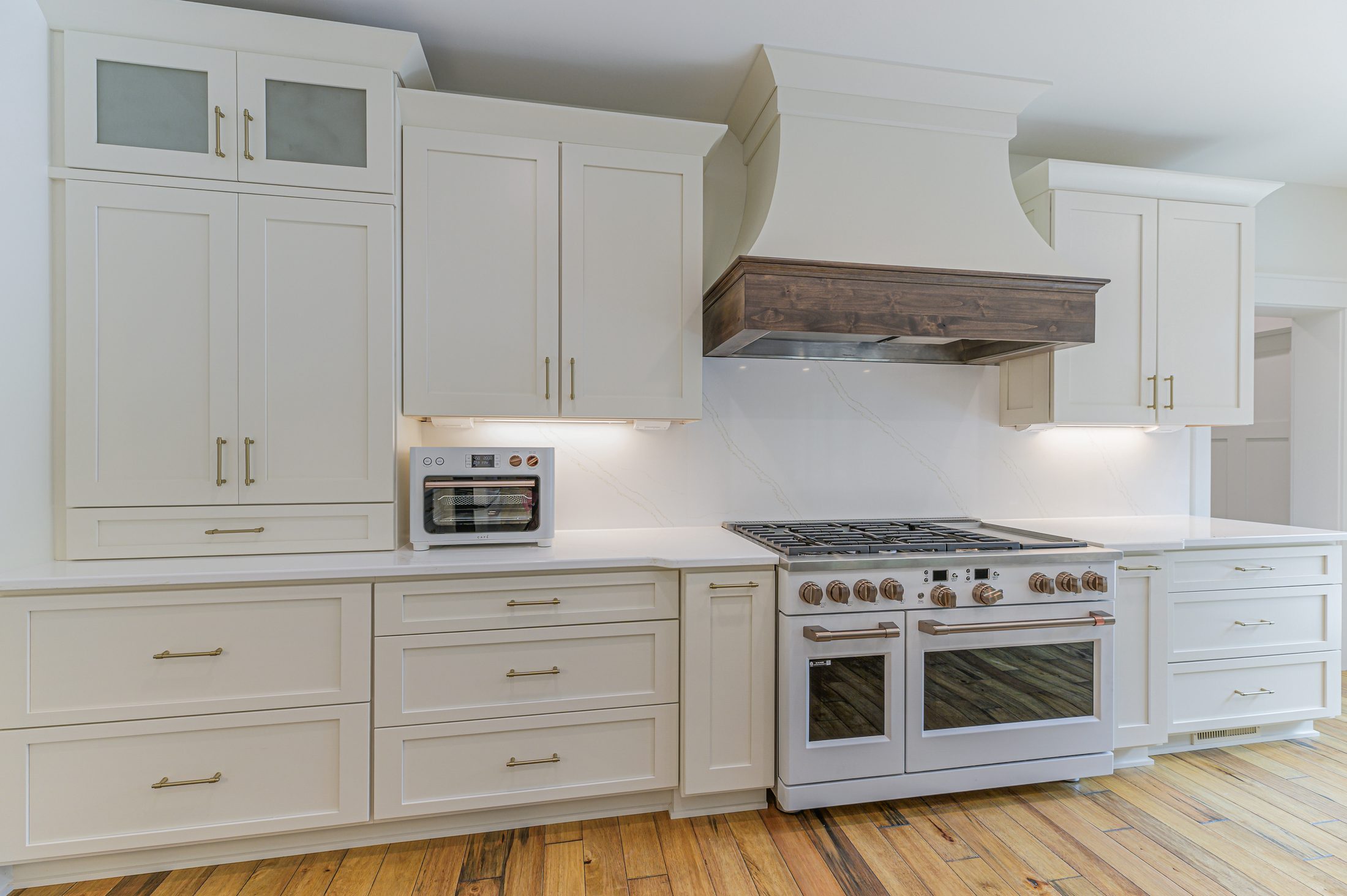 White kitchen cabinetry, professional range, and stained wood hood detail