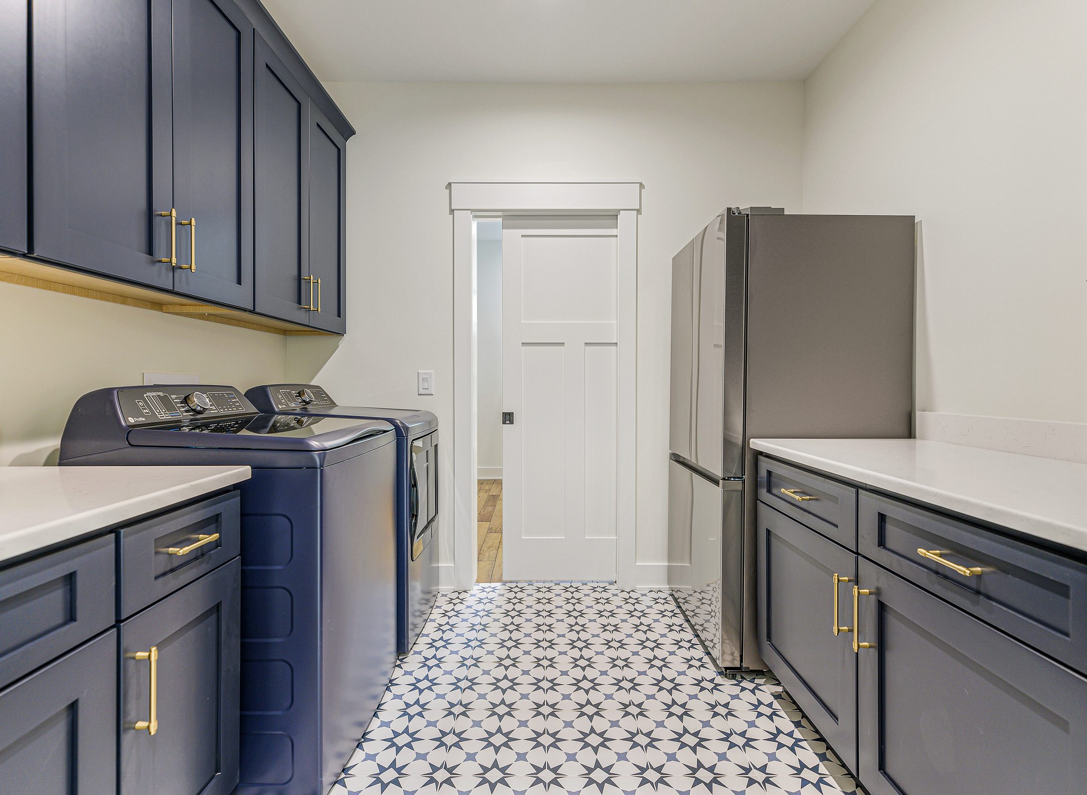 Laundry room with blue cabinetry and patterned tile floor in a Arbor Creek custom home in West End